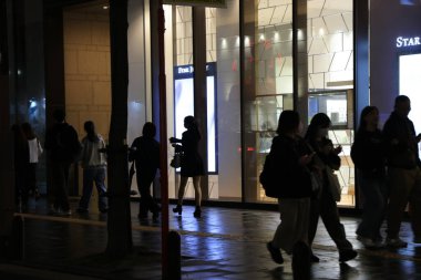 Alışveriş merkezi geceleri aydınlanıyor, insanlar yürüyor ve bisiklete biniyor.