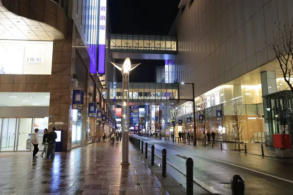 Alışveriş merkezi geceleri aydınlanıyor, insanlar yürüyor ve bisiklete biniyor.