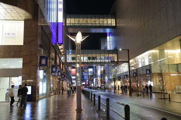 Alışveriş merkezi geceleri aydınlanıyor, insanlar yürüyor ve bisiklete biniyor.