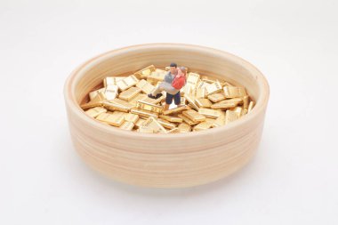 Tahtaya yerleştirilmiş altın külçelerin arasında duran küçük bir figürün yakın çekimi.