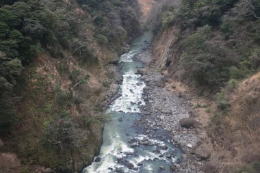 Engebeli bir vadi boyunca, engebeli arazi ve yemyeşil bitki örtüsüyle çevrili.
