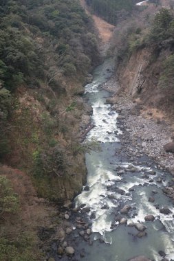 Engebeli bir vadi boyunca, engebeli arazi ve yemyeşil bitki örtüsüyle çevrili.