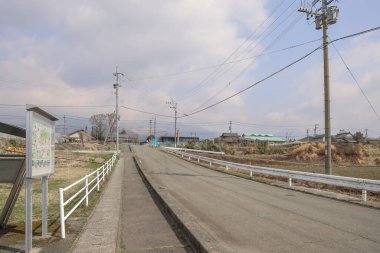 Çevresindeki yeşil alanlar ve elektrik direkleri olan sakin bir kırsal yol.