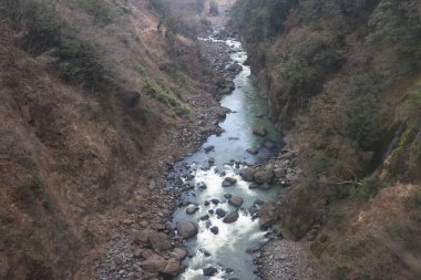 Engebeli bir vadi boyunca, engebeli arazi ve yemyeşil bitki örtüsüyle çevrili.