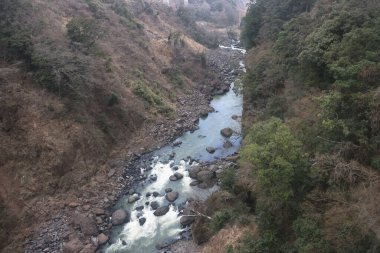 Engebeli bir vadi boyunca, engebeli arazi ve yemyeşil bitki örtüsüyle çevrili.