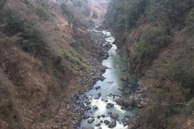 Engebeli bir vadi boyunca, engebeli arazi ve yemyeşil bitki örtüsüyle çevrili.