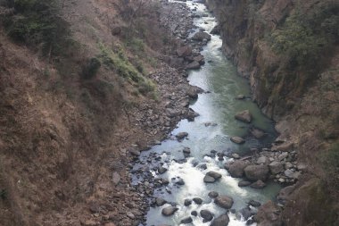 Engebeli bir vadi boyunca, engebeli arazi ve yemyeşil bitki örtüsüyle çevrili.