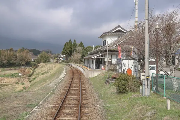 Geleneksel bir evin yanında kırsal tren raylarının kıvrımlı olduğu sakin bir manzara