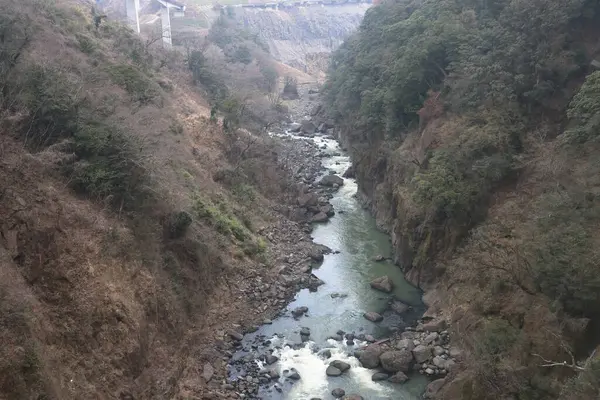 Engebeli bir vadi boyunca, engebeli arazi ve yemyeşil bitki örtüsüyle çevrili.