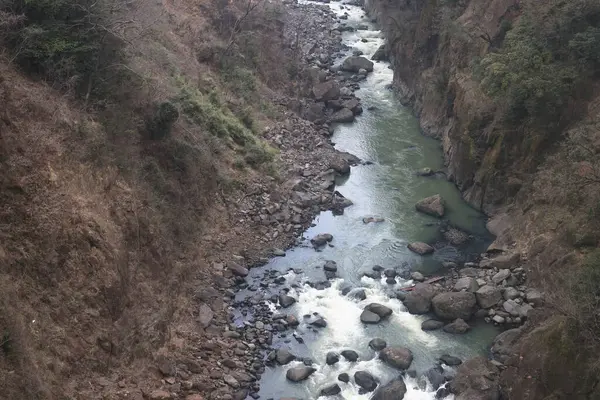 Engebeli bir vadi boyunca, engebeli arazi ve yemyeşil bitki örtüsüyle çevrili.