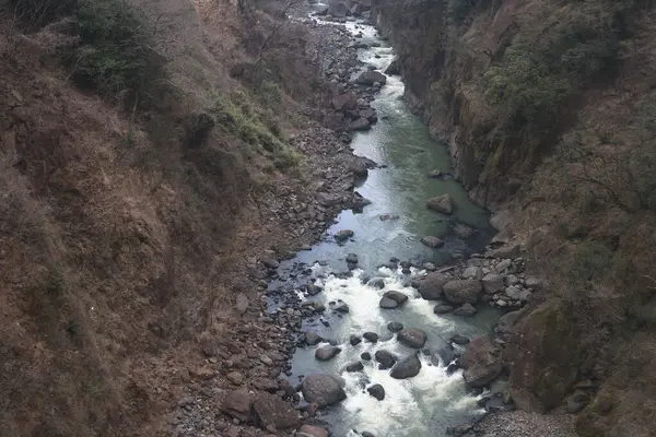 Engebeli bir vadi boyunca, engebeli arazi ve yemyeşil bitki örtüsüyle çevrili.