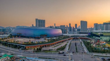 Mimari bina gün batımında aydınlandı, bir hareketlilik ile çevrili.