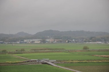Serin manzara uzak tepelerle yemyeşil tarlalar sergiliyor