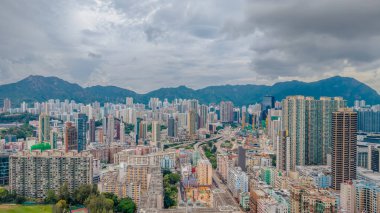 Dramatik bulutlu gökyüzünün altında manzaralı dağlarla çevrili binalar..