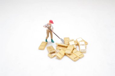 Altın külçelerle çevrili bir aleti tutan bir işçinin heykeli.