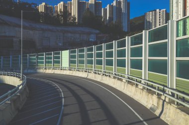 Ses bariyerleriyle çevrili ve yüksek binalarla çevrili kıvrımlı bir şehir yolu.