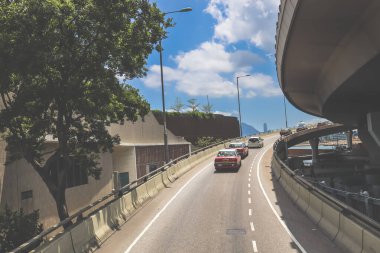 Kavisli bir karayolu, araçlar ve manzaralı bir şehir silueti içeren şehir yolu.