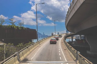 Kavisli bir karayolu, araçlar ve manzaralı bir şehir silueti içeren şehir yolu.