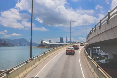 Kavisli bir karayolu, araçlar ve manzaralı bir şehir silueti içeren şehir yolu.