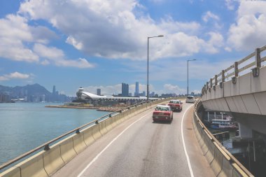 Kavisli bir karayolu, araçlar ve manzaralı bir şehir silueti içeren şehir yolu.