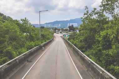 Çevresi yeşilliklerle çevrili, bakımlı bir otoyol boyunca giden araçlar.