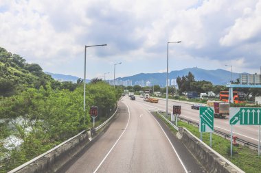 Çevresi yeşilliklerle çevrili, bakımlı bir otoyol boyunca giden araçlar.