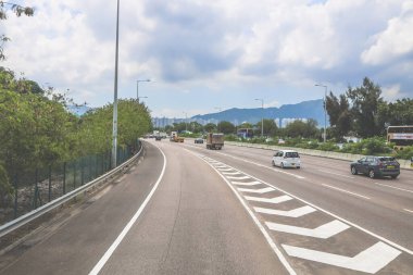 Çevresi yeşilliklerle çevrili, bakımlı bir otoyol boyunca giden araçlar.