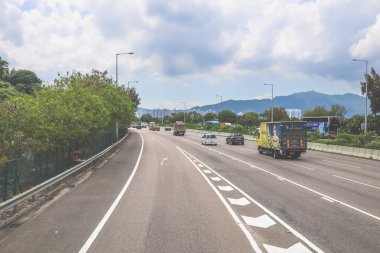 Çevresi yeşilliklerle çevrili, bakımlı bir otoyol boyunca giden araçlar.