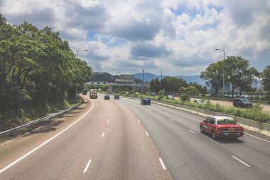 Çevresi yeşilliklerle çevrili, bakımlı bir otoyol boyunca giden araçlar.