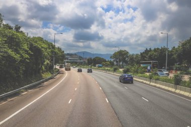 Çevresi yeşilliklerle çevrili, bakımlı bir otoyol boyunca giden araçlar.