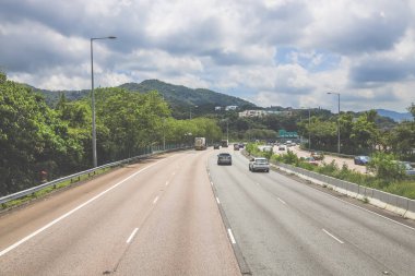 Çevresi yeşilliklerle çevrili, bakımlı bir otoyol boyunca giden araçlar.