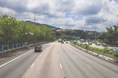 Çevresi yeşilliklerle çevrili, bakımlı bir otoyol boyunca giden araçlar.
