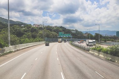 Çevresi yeşilliklerle çevrili, bakımlı bir otoyol boyunca giden araçlar.