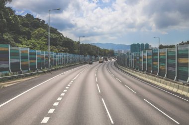 Çevresi yeşilliklerle çevrili, bakımlı bir otoyol boyunca giden araçlar.