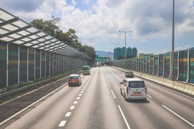 Çevresi yeşilliklerle çevrili, bakımlı bir otoyol boyunca giden araçlar.