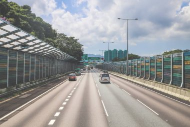 Çevresi yeşilliklerle çevrili, bakımlı bir otoyol boyunca giden araçlar.