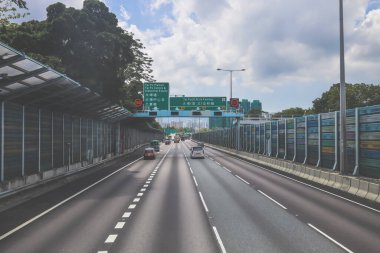 Çevresi yeşilliklerle çevrili, bakımlı bir otoyol boyunca giden araçlar.