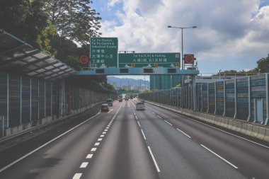 Çevresi yeşilliklerle çevrili, bakımlı bir otoyol boyunca giden araçlar.