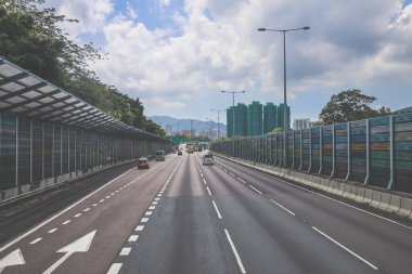 Çevresi yeşilliklerle çevrili, bakımlı bir otoyol boyunca giden araçlar.
