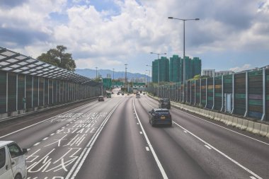Çevresi yeşilliklerle çevrili, bakımlı bir otoyol boyunca giden araçlar.