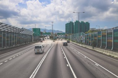 Çevresi yeşilliklerle çevrili, bakımlı bir otoyol boyunca giden araçlar.