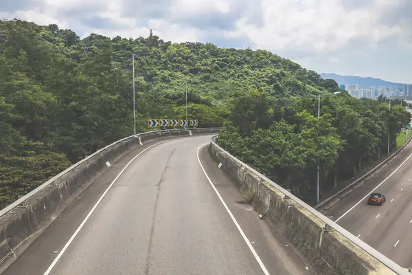 Çevresi yeşilliklerle çevrili, bakımlı bir otoyol boyunca giden araçlar.