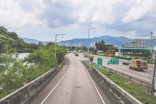 Çevresi yeşilliklerle çevrili, bakımlı bir otoyol boyunca giden araçlar.