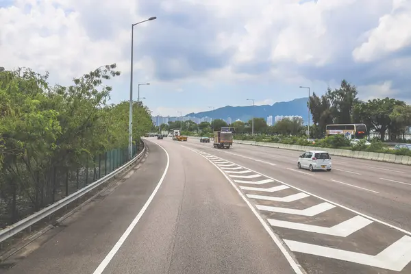 Çevresi yeşilliklerle çevrili, bakımlı bir otoyol boyunca giden araçlar.