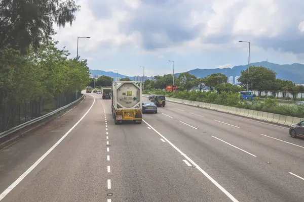 Çevresi yeşilliklerle çevrili, bakımlı bir otoyol boyunca giden araçlar.