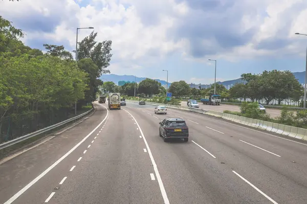 Çevresi yeşilliklerle çevrili, bakımlı bir otoyol boyunca giden araçlar.