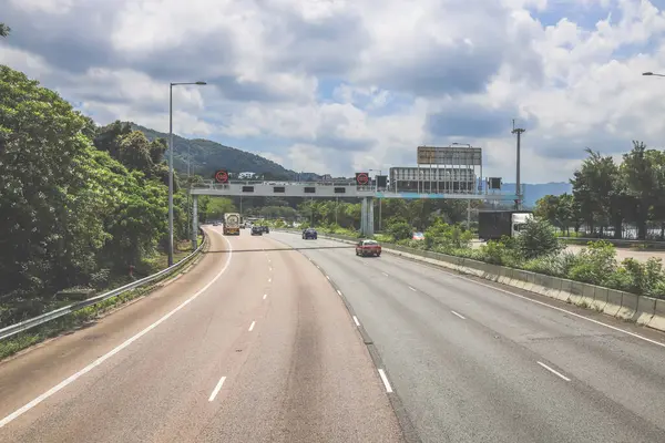 Çevresi yeşilliklerle çevrili, bakımlı bir otoyol boyunca giden araçlar.