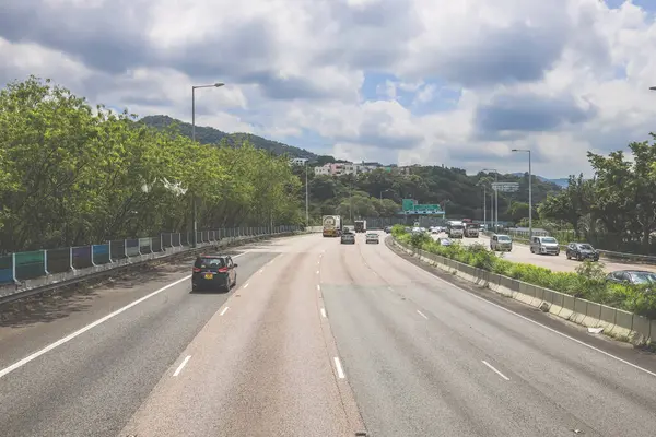 Çevresi yeşilliklerle çevrili, bakımlı bir otoyol boyunca giden araçlar.