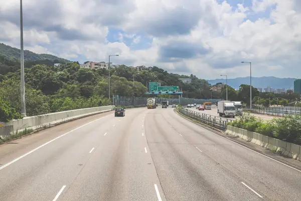 Çevresi yeşilliklerle çevrili, bakımlı bir otoyol boyunca giden araçlar.