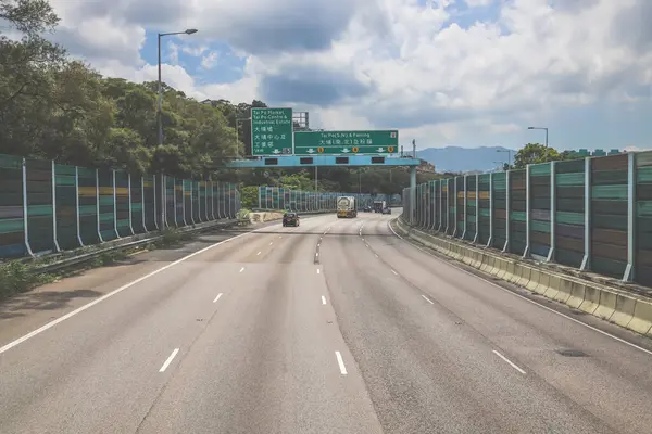 Çevresi yeşilliklerle çevrili, bakımlı bir otoyol boyunca giden araçlar.